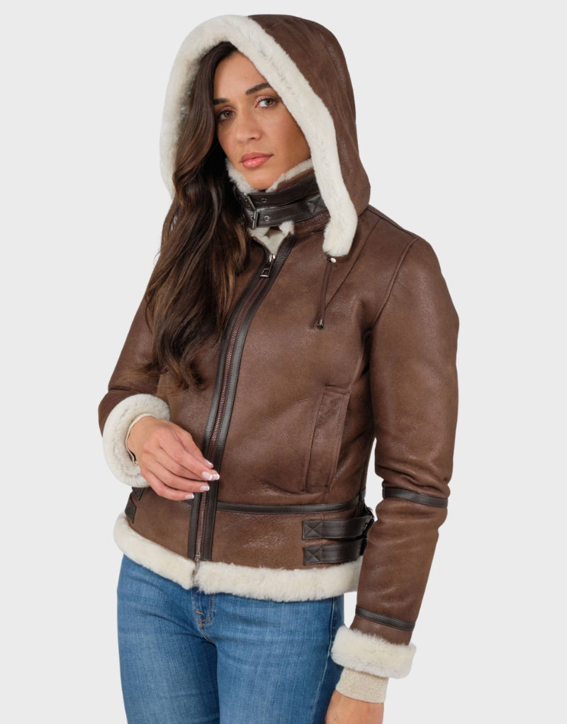 Women's brown leather jacket with white shearling lining, zip-up hoodie, adjustable buckle collar, and fur-trimmed cuffs and hem perfect for winter warmth and style.