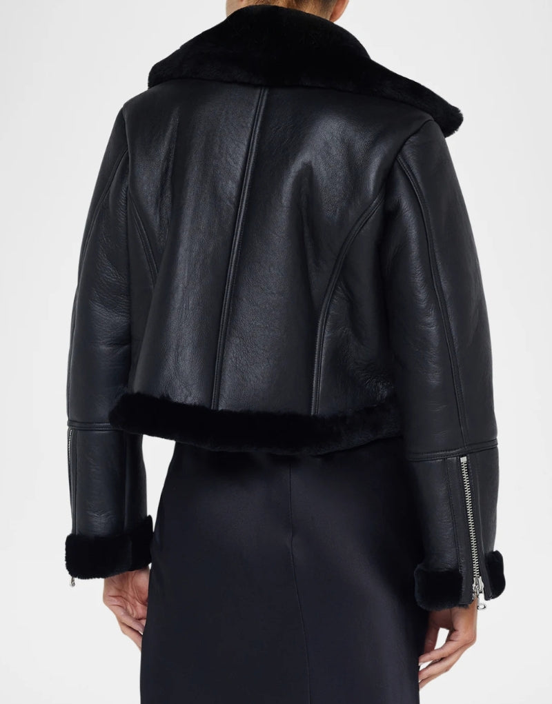 Back view of a black leather shearling jacket featuring a cropped design, fur-lined collar, and zippered cuffs modern and elegant winter fashion.