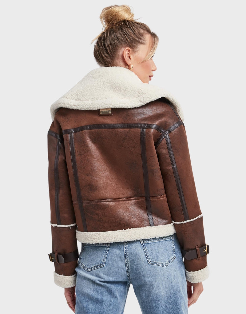 Vintage-inspired cropped aviator jacket in brown leather with shearling lining, featuring zip closures and adjustable waist straps for a chic winter look.