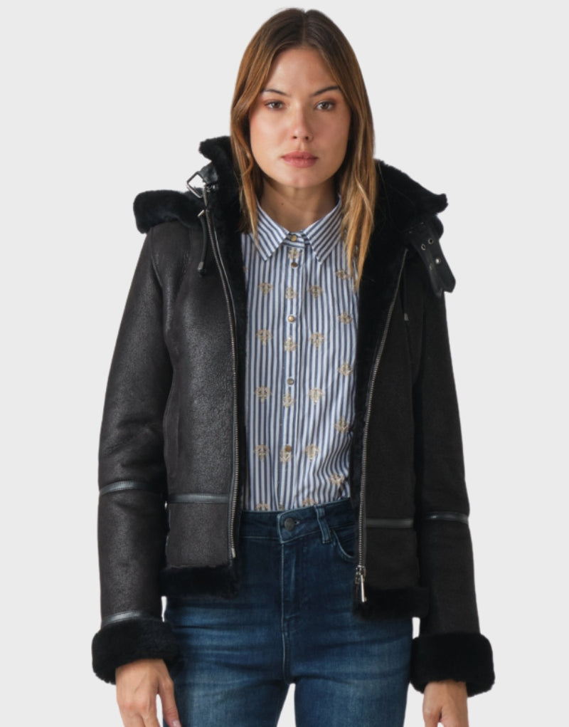 Women's black sheepskin shearling jacket with a fur-lined hood, zip-up front, and adjustable waist straps perfect for winter warmth and style.